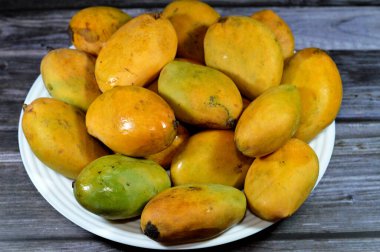 Plate of Egyptian fresh mango fruit with tropical delicacy, mangoes are nutritionally rich fruit with distinctive flavor, smell, taste, selective focus of Awaisy or Ewes Mango fruit isolated on wood