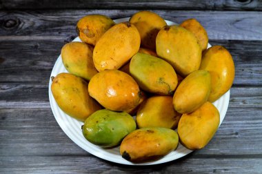 Plate of Egyptian fresh mango fruit with tropical delicacy, mangoes are nutritionally rich fruit with distinctive flavor, smell, taste, selective focus of Awaisy or Ewes Mango fruit isolated on wood