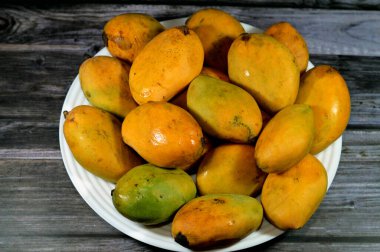 Plate of Egyptian fresh mango fruit with tropical delicacy, mangoes are nutritionally rich fruit with distinctive flavor, smell, taste, selective focus of Awaisy or Ewes Mango fruit isolated on wood