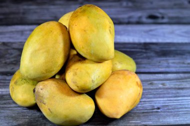 Pile of Egyptian fresh mango fruit with tropical delicacy, mangoes are nutritionally rich fruit with distinctive flavor, smell, taste, selective focus of Awaisy or Ewes Mango fruit isolated on wood