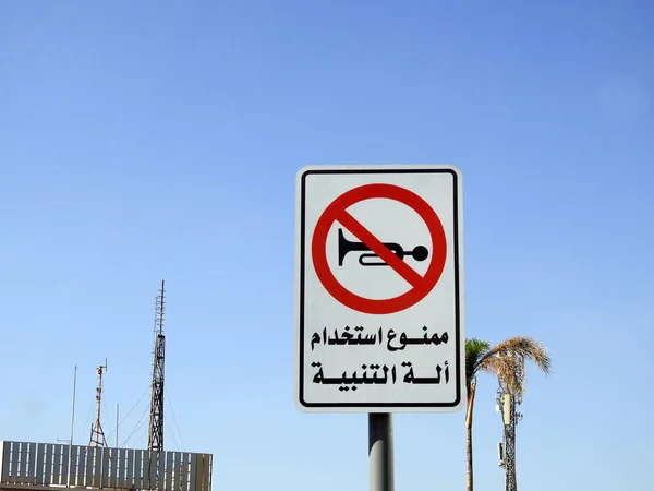 A traffic sign at the side of the road, Translation of the Arabic text (Car horn is not allowed), a forbidden zone area to use the car horn sound, crossed out red sign car sound horns prohibited