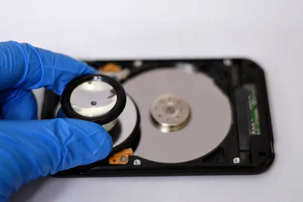 A medical stethoscope on HDD platters and spindle motor, hard disk drive disassembled damaged components, computer maintenance, running diagnostics, recovery, data erase, data killer software concept
