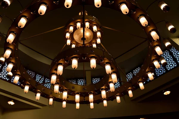 Büyük, dairesel bir cami avizesi lambalı, bakır ve diğer metallerden yapılmış, caminin içindeki büyük cami kubbesine sabitlenmiş, caminin ana aydınlatmasını sağlayan bir tavan lambası.