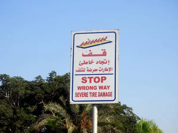 A warning road sign in Arabic and English, Translation of Arabic words ( Stop, Wrong way, Severe Tire Damage ) as a caution before a spikes barrier on the road that will cause Tyre damage  on that way