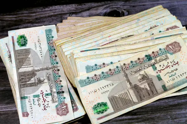 Stack of Egyptian currency of 100 EGP LE one hundred Egyptian pound bills, spending, giving and using money concept, paying and buying using banknotes with Sultan Hassan mosque and the Sphinx