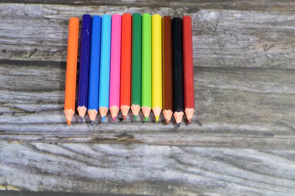 small short wood color pencils of different colors for painting isolated on wooden background, back to school concept, school supplies and education background, selective focus