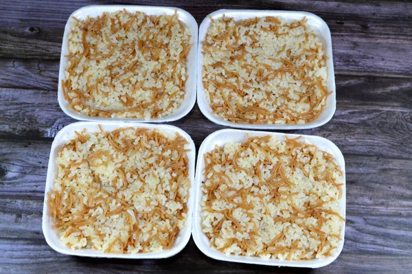 Egyptian rice with vermicelli cooked on hot steam served in a disposable plate and isolated on wooden background, the vermicelli is first grilled in oil or ghee then the white rice then added, cooked