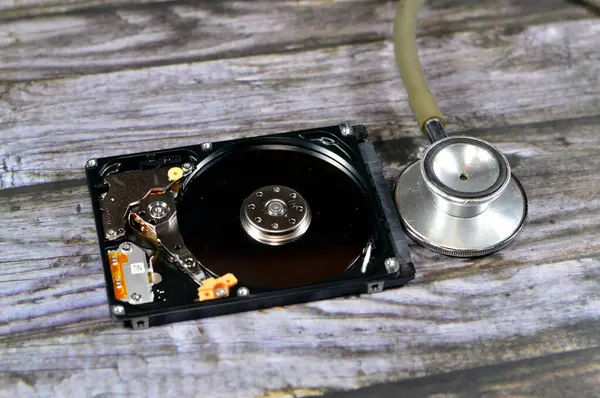 A medical stethoscope on a laptop 2.5 inch hard disk drive storage memory, repair broken computer part, an open hard disc with platters, spindle, actuator and read, write head, HDD diagnostic tool