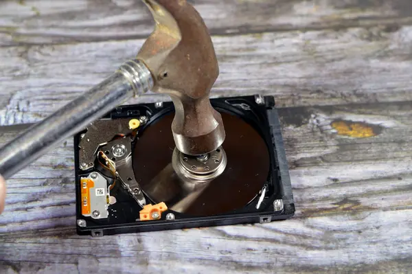 A Hammer on a laptop 2.5 inch hard disk drive storage memory, repair broken computer part, an open hard disc with platters, spindle, actuator and read, write head, HDD erase and kill data tool