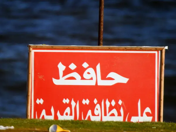 Translation of the Arabic text (Keep the place clean), an information board on the beach of a resort, informing people to keep the place clean while there are rubbish and wastes beside the sign