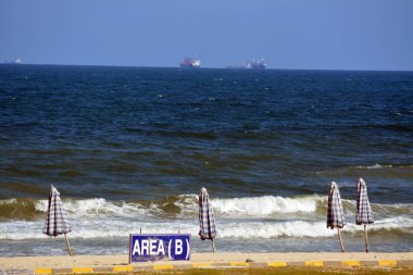 İskenderiye plajı, dalgalı ve kumlu sahil, tatil zamanı insanların tatillerinde eğlenmesi için, Akdeniz ve denizden önce yeşil bahçeler, seçici bir şekilde odaklanmaları için.