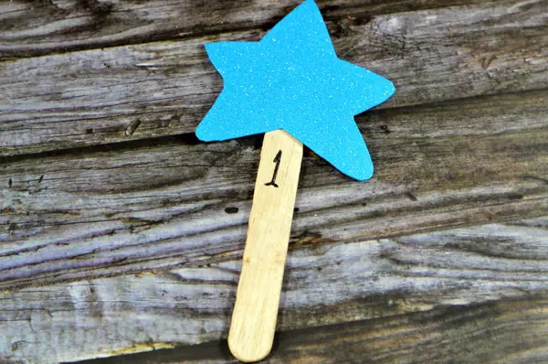 A yellow star fixed to a wooden tongue depressor with number 1 as a reward for school child, glittered colorful Eva foam sheets, colored cardboard, rubber pad, sponge papers for school arts and crafts