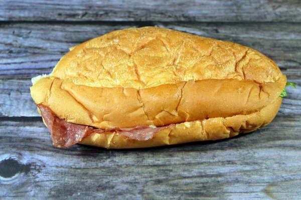 Salami slices sandwich in a long bun bread with lettuce and mayonnaise, Salami is a cured sausage consisting of fermented and air-dried meat, as a filling of bun served as a snack with melted cheese