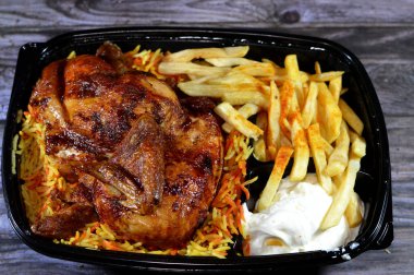Arap mutfağından ızgara ızgara tavuk rengarenk Basmati pilavı ve patates kızartması sarımsak sosuyla servis edilen siyah bir tek kullanımlık tabakta servis ediliyor.