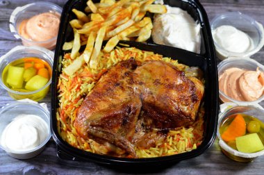 Arap mutfağından ızgara ızgara tavuk rengarenk Basmati pilavı ve patates kızartması sarımsak sosuyla servis edilen siyah bir tek kullanımlık tabakta servis ediliyor.