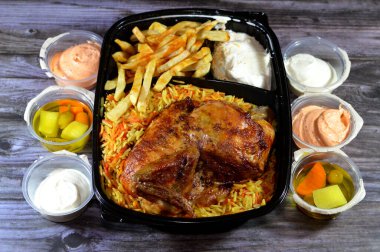 Arap mutfağından ızgara ızgara tavuk rengarenk Basmati pilavı ve patates kızartması sarımsak sosuyla servis edilen siyah bir tek kullanımlık tabakta servis ediliyor.