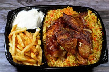 Arap mutfağından ızgara ızgara tavuk rengarenk Basmati pilavı ve patates kızartması sarımsak sosuyla servis edilen siyah bir tek kullanımlık tabakta servis ediliyor.