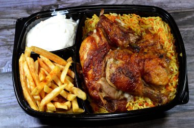 Arap mutfağından ızgara ızgara tavuk rengarenk Basmati pilavı ve patates kızartması sarımsak sosuyla servis edilen siyah bir tek kullanımlık tabakta servis ediliyor.