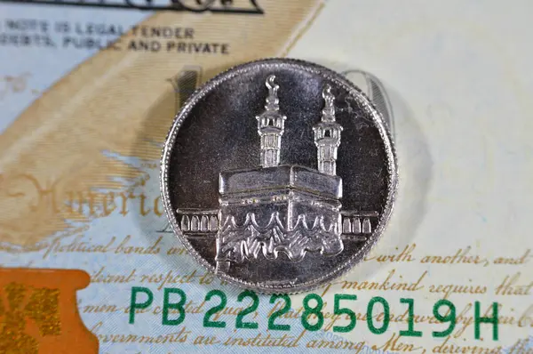 stock image A close up of an Islamic pound coin of pure precious silver metal features Kaaba and Masjid Al Haram mosque in Mecca in Saudi Arabia kingdom, on 100 USD American dollars bill cash money