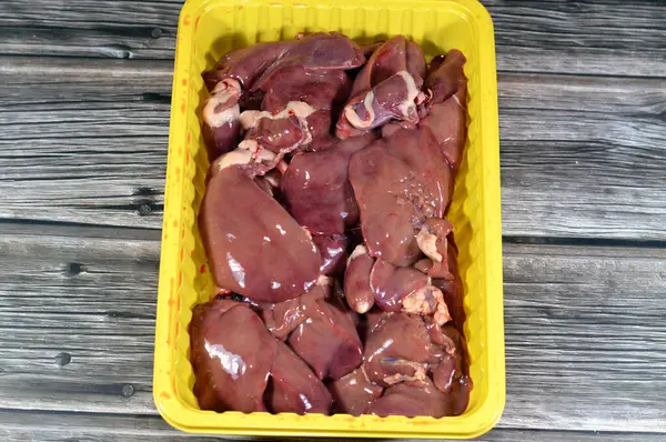 Raw chicken livers, gizzards and hearts, fresh liver, gizzard and heart of chickens full of protein in a yellow disposable plate isolated on wooden background ready to be cooked, selective focus