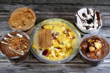 Çeşit çeşit çikolatalı profiterollerin arkaplanı, bisküvili kremalı krema, sütlü puding tatlı karışımı qishta, basbousa, mango suyu, elma parçaları, süt ve şeker.