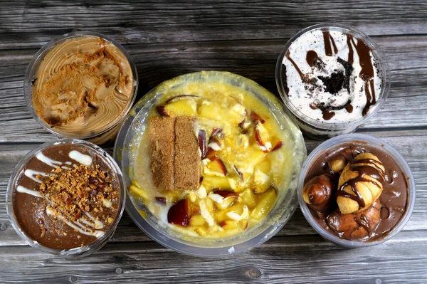 Çeşit çeşit çikolatalı profiterollerin arkaplanı, bisküvili kremalı krema, sütlü puding tatlı karışımı qishta, basbousa, mango suyu, elma parçaları, süt ve şeker.