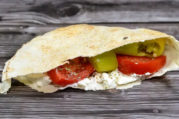 Traditional Shami flat bread made of wheat and flour stuffed with white creamy cheese, slices of tomatoes, pieces of green chili peppers and thyme herb, a cheese sandwich in shami bread with vegetable