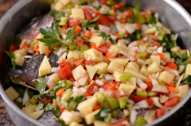 Tilapia balığı Oreochromis niloticus 'u domates, patates, havuç, kereviz, soğan, baharat, kimyon, karabiber ve tuz dilimleri ile karıştırır ve bir tepside fırında pişirilmeye hazırdır.