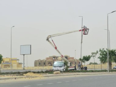 Kahire, Mısır, 10 Mayıs 2024: Bir sokak lambası direğinin bakım ve onarımı bir kova boom lift hidrolik kamyon ile, elektrikçi bakım aracının platformunda bir sokak lambasını tamir ediyor.