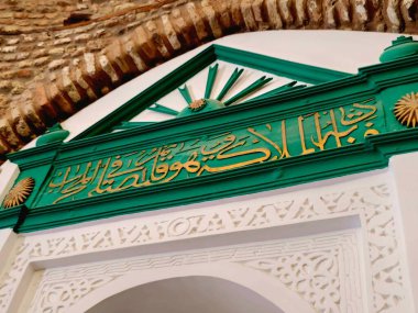 Arapça çevirisi (O ayaktayken melekler ona şöyle der:) Medine 'nin en eski camilerinden biri olan ve peygamber camii yakınlarında bulunan Ebu Bekir Camii' ndeki Mescid Abo Bekir as-Siddiq.