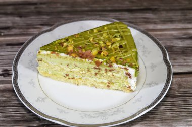 Fıstıklı, üçgen, süngerimsi kek dilimi. İçi şam fıstıklı krema ve krema katmanları ile kaplı. Katmanlar halinde pasta, bir tabakta servis edilir ve ahşap arka planda izole edilir.