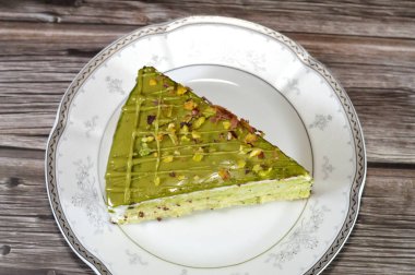 Fıstıklı, üçgen, süngerimsi kek dilimi. İçi şam fıstıklı krema ve krema katmanları ile kaplı. Katmanlar halinde pasta, bir tabakta servis edilir ve ahşap arka planda izole edilir.