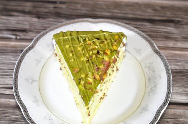 Fıstıklı, üçgen, süngerimsi kek dilimi. İçi şam fıstıklı krema ve krema katmanları ile kaplı. Katmanlar halinde pasta, bir tabakta servis edilir ve ahşap arka planda izole edilir.