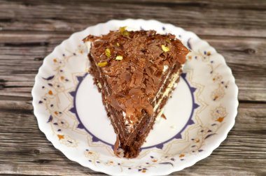 Çikolata üçgen şeklinde rendelenmiş süngerimsi kek dilimi kademeli çikolatalarla doldurulmuş ve krem şanti katmanlarıyla doldurulmuş, bir tabakta servis edilmiş ve ahşap arka planda izole edilmiş.