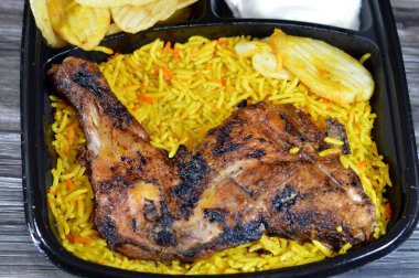 Arabic Syrian cuisine of charcoal grilled barbecued chicken with colorful Basmati rice and fried chips potatoes, served in a black disposable plate, served with regular and spicy garlic sauce clipart