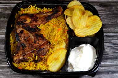 Arabic Syrian cuisine of charcoal grilled barbecued chicken with colorful Basmati rice and fried chips potatoes, served in a black disposable plate, served with regular and spicy garlic sauce