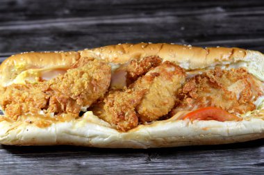 Kızarmış tavuk parçaları füme hindi dilimleri, marul, domates, çedar ve büyük lezzetli sos susamlı uzun bir çörek, batı sandviçi tavuk parçaları, hindi, sebze, sos ile dolu.