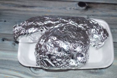 Alüminyum folyoya sarılı fast food sandviçleri, Burger sandviçi ve kızarmış patates parmakları ve turşulu, ketçaplı ve mayonezli uzun bir çöreğin içinde seçici bir odak noktası.