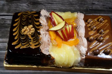 Kutlamalar, koyu çikolata, karamel, çırpılmış vanilya kreması, ananas, elma, şeftali ve fındık dilimleri için üç parçadan oluşan dikdörtgen şeklinde doğum günü pastası.