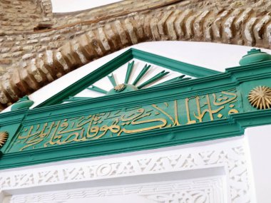 Arapça çevirisi (O ayaktayken melekler ona şöyle der:) Medine 'nin en eski camilerinden biri olan ve peygamber camii yakınlarında bulunan Ebu Bekir Camii' ndeki Mescid Abo Bekir as-Siddiq.