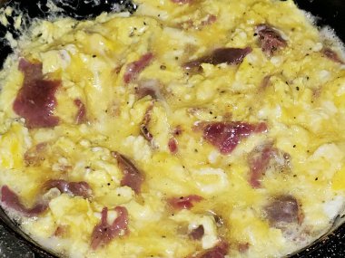 Scrambled eggs with pastrami, a dish made from eggs stirred, whipped or beaten together while being gently heated, with salt, butter, oil and black pepper with slices and pieces of beef pastrami