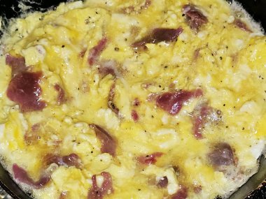 Scrambled eggs with pastrami, a dish made from eggs stirred, whipped or beaten together while being gently heated, with salt, butter, oil and black pepper with slices and pieces of beef pastrami