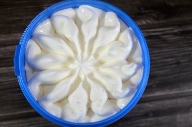Tahta arka planda izole edilmiş plastik bir kasede dondurulmuş vanilyalı dondurma servis edilmeye hazır mavi kapta çiçek şeklinde vanilyalı dondurma seçici bir odak noktası.