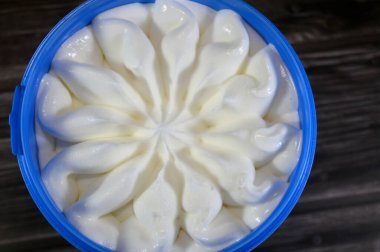 Tahta arka planda izole edilmiş plastik bir kasede dondurulmuş vanilyalı dondurma servis edilmeye hazır mavi kapta çiçek şeklinde vanilyalı dondurma seçici bir odak noktası.