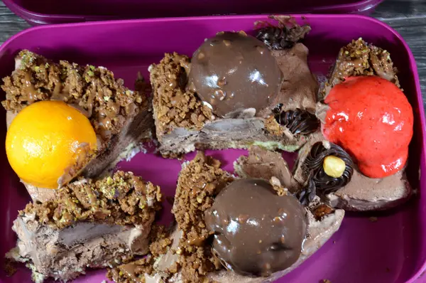 Bir parça dondurmalı kek, üzerinde çikolata topu ve krema, karamel sosu, fındıklı çikolata parçaları, fındıklı fındık, mango ve çilekli toplar, yaz ve tatil kavramı.