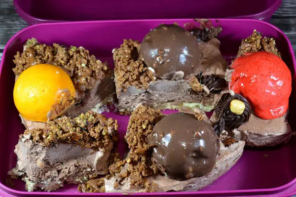 Bir parça dondurmalı kek, üzerinde çikolata topu ve krema, karamel sosu, fındıklı çikolata parçaları, fındıklı fındık, mango ve çilekli toplar, yaz ve tatil kavramı.