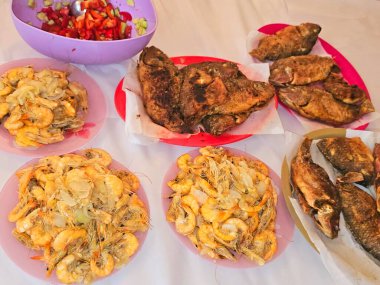 Kızarmış Nil tilapia balığının deniz mahsulleri Oreochromis Niloticus kızartması, kızgın buharda pişirilmiş kabuksuz gri karidesler ve soğan, sarımsaklı kimyon ve yeşil salatayla ızgara.