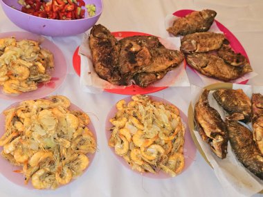 Kızarmış Nil tilapia balığının deniz mahsulleri Oreochromis Niloticus kızartması, kızgın buharda pişirilmiş kabuksuz gri karidesler ve soğan, sarımsaklı kimyon ve yeşil salatayla ızgara.