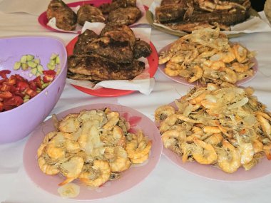 Kızarmış Nil tilapia balığının deniz mahsulleri Oreochromis Niloticus kızartması, kızgın buharda pişirilmiş kabuksuz gri karidesler ve soğan, sarımsaklı kimyon ve yeşil salatayla ızgara.