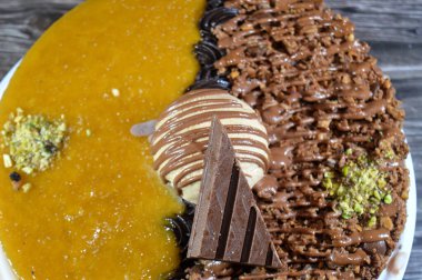 Dondurmalı pasta, üzerinde çikolata parçacıkları ve krema ve sos ile kaplı, fıstıklı çikolata parçaları, yarım mango ve yarım çikolata, yaz ve tatil konsepti.
